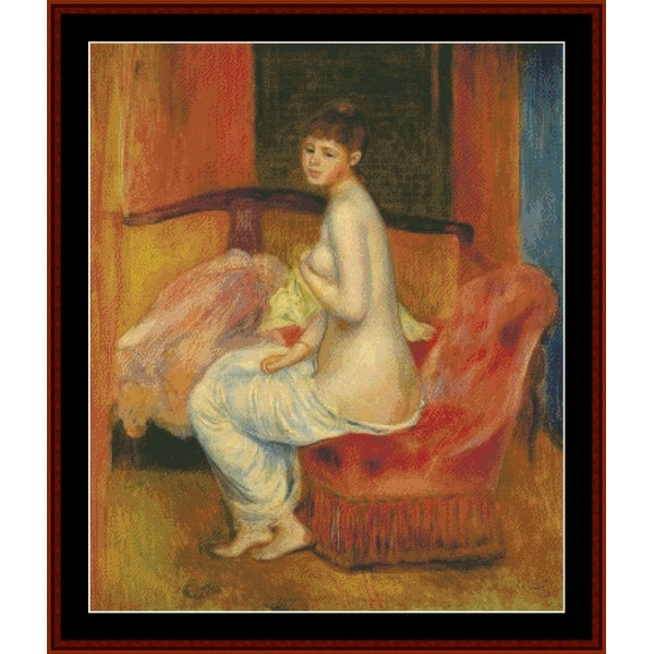 Counted Cross Stitch Pattern – Seated Nude, 1885 by Pierre Auguste Renoir - Cross Stitch Collectibles - A framed impressionist-style painting depicting a nude seated woman on a red upholstered chair, with warm orange, yellow, and brown tones and a dark central background.
