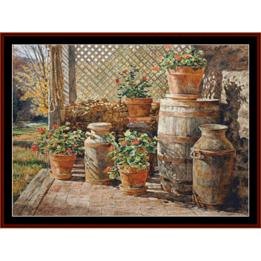 Counted Cross Stitch Pattern – October Shadow, Americana - Cross Stitch Collectibles - A framed art print depicting a rustic outdoor patio scene with potted red flowers, terracotta pots, wooden barrels, and vintage metal milk cans on a brick floor.