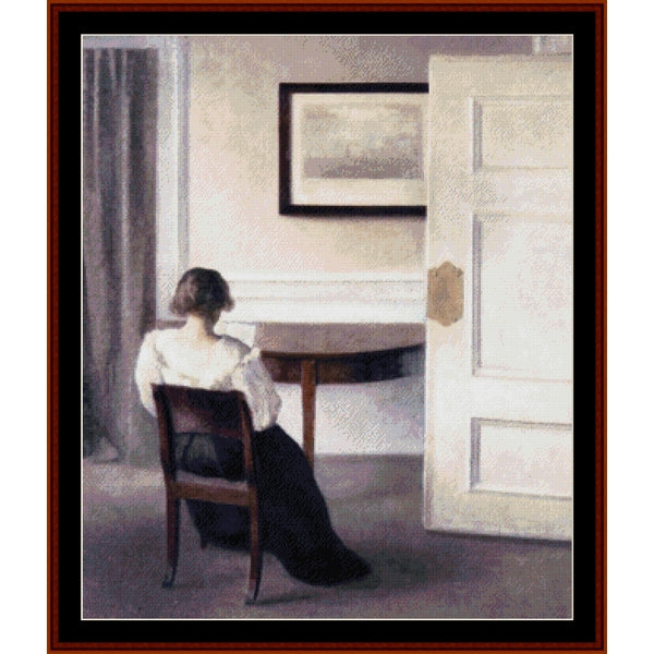 Counted Cross Stitch Pattern by Cross Stitch Collectibles - Woman sitting at a table in a room with a painting on the wall.
