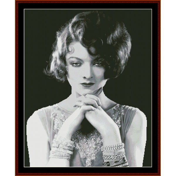 Counted Cross Stitch Pattern: Myrna Loy II, Vintage Celebrity - Cross Stitch Collectibles - A framed black and white portrait print of a woman with short curled hair, wearing a beaded top and bracelets, set against a dark background