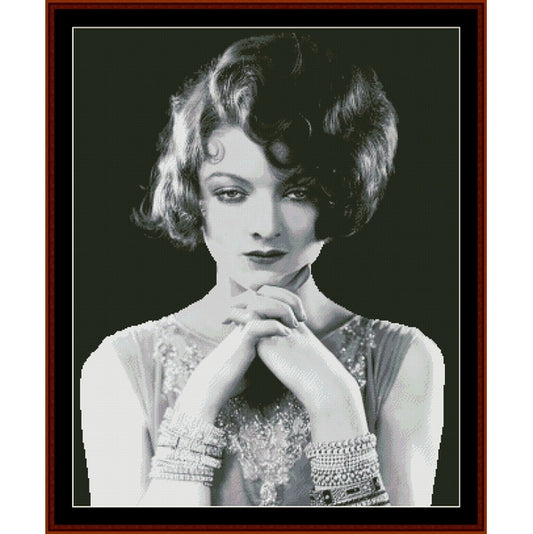 Counted Cross Stitch Pattern: Myrna Loy II, Vintage Celebrity - Cross Stitch Collectibles - A framed black and white portrait print of a woman with short curled hair, wearing a beaded top and bracelets, set against a dark background