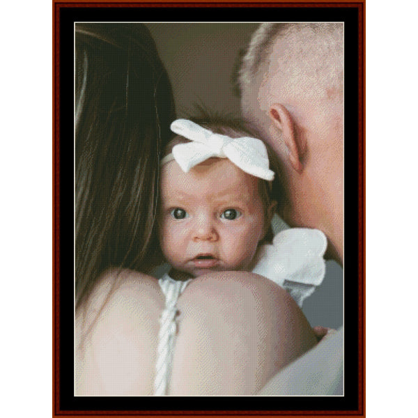 Custom pdf counted cross stitch pattern by Cross Stitch Collectibles - A framed portrait-style photo print showing a baby wearing a white bow headband, held by an adult with long dark hair and another person